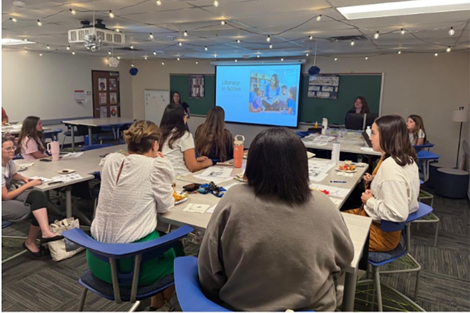 Participants sit in a classroom, looking at a screen.