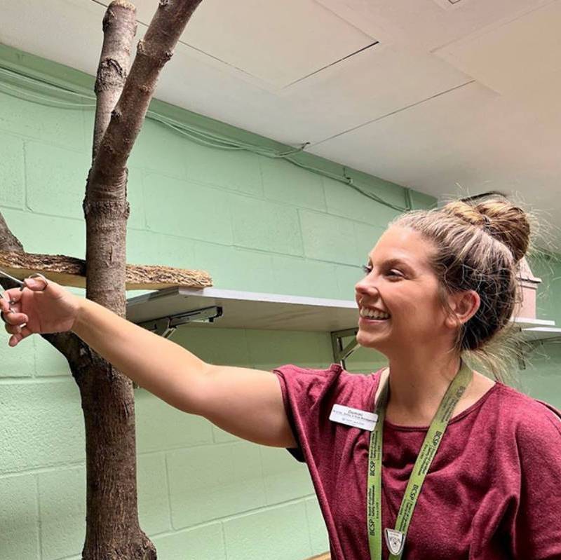 An alumni smiles to the side of the camera while reaching at something outside of the frame.