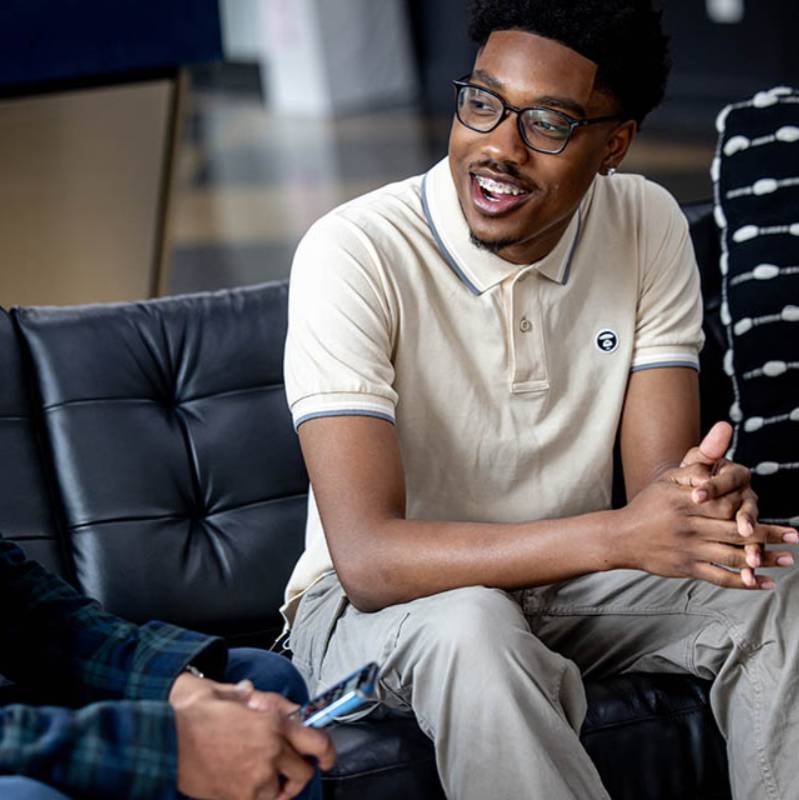 A student sits on a couch engaged in conversation.