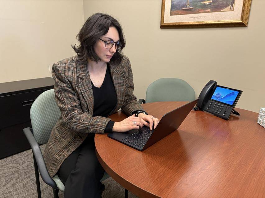 Clinic student Shannon Besch sits at a table on her computer in the legal clinics Clinic student Shannon Besch works on a laptop at a table in an office.