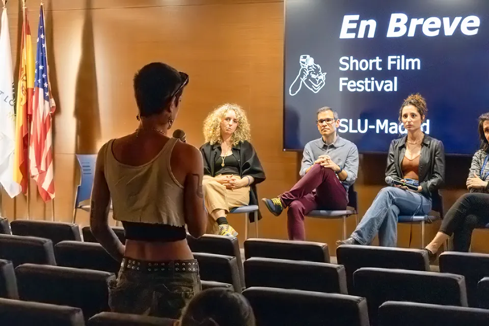 Girl holds a microphone while standing up in auditorium and faces film festival judges who are sitting on the stage.