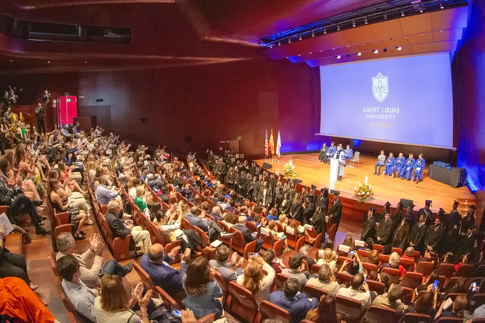 A speaker stands on-stage at a lectern while audience members watch during a commencement ceremony