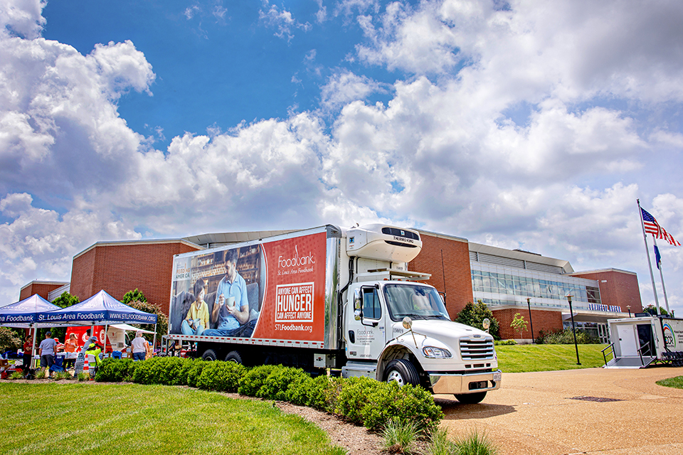 A box truck that reads "Foodbank: St. Louis Area Foodbank. Anyone can affect hunger. Hunger can affect anyone. stlfoodbank.org" is parked on the sidewalk in front of the Chaifetz Arena on SLU's campus. 