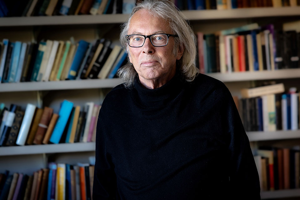 Jonathan Sawday, Ph.D., poses for a photo wearing a long-sleeved shirt and black glasses. A bookshelf is behind him.