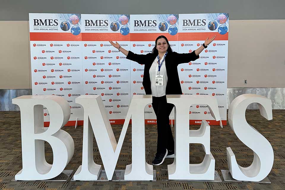 A student researcher stands in front of giant letters that read BMES.